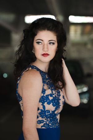 Elegant blue lace evening gown with sheer floral details photographed in dramatic lighting.