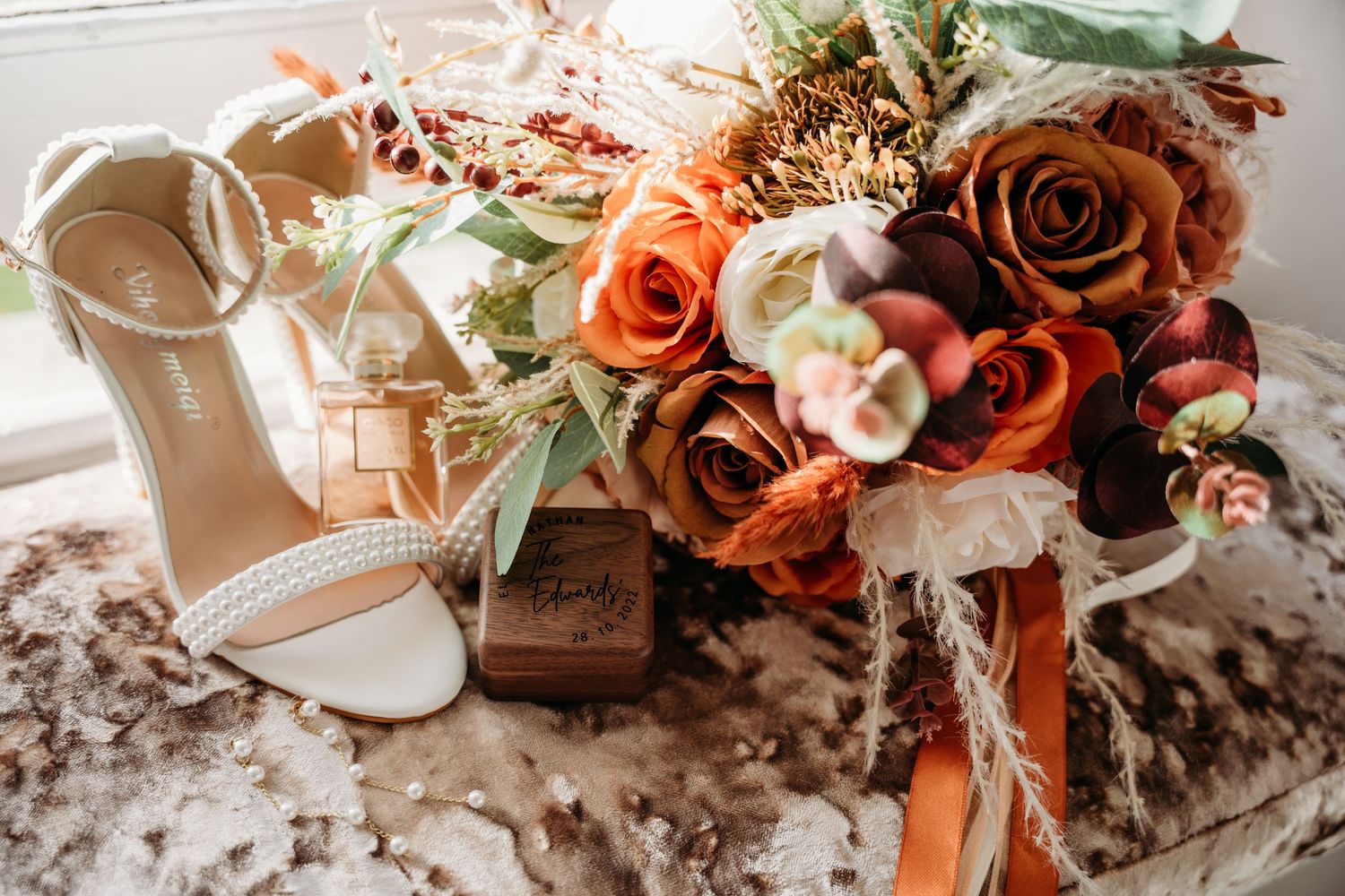 Wedding accessories featuring orange and white roses with bridal shoes on textured surface.