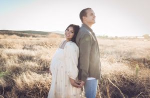 A couple stands back to back in a sunlit field of dry grass during golden hour.