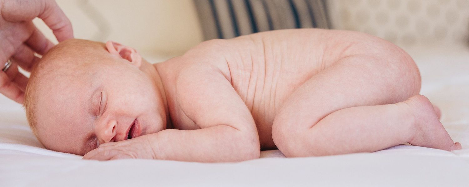Peaceful sleeping newborn photographed on soft white bedding in natural light.
