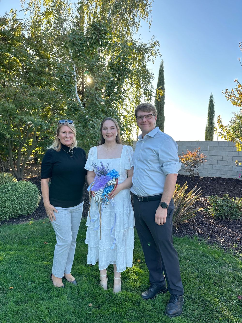 Amidst the lush green grass, three figures gather for a wedding rehearsal, their joy accentuated by the flowers