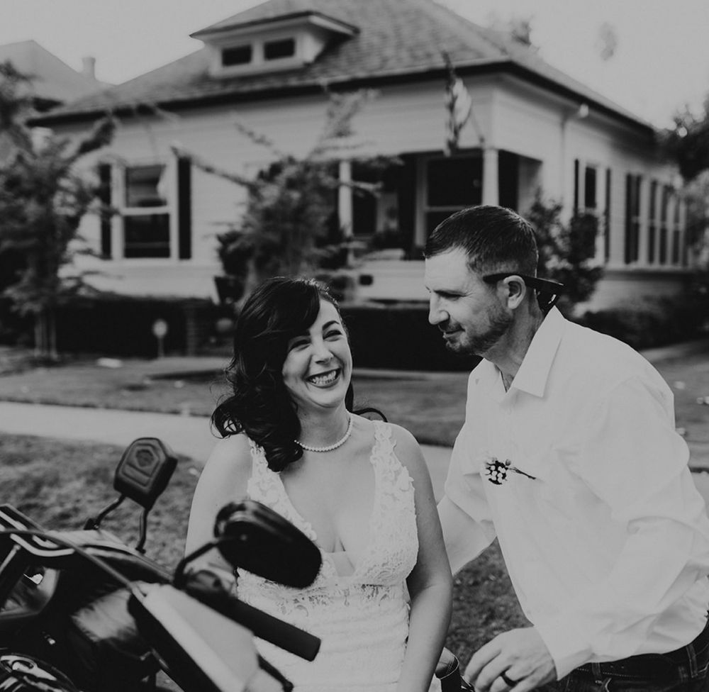 Newlyweds happily pose beside a motorcycle during their backyard wedding