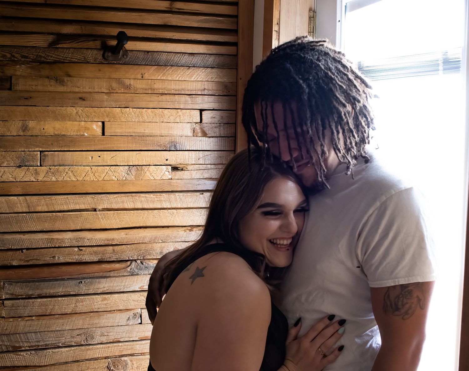 A tender moment between a couple against a wooden paneled wall in natural lighting.