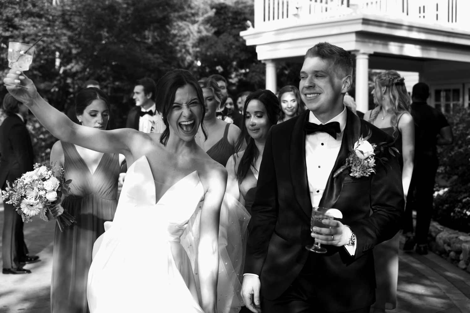 Black and white photo of joyful wedding party celebration outdoors.
