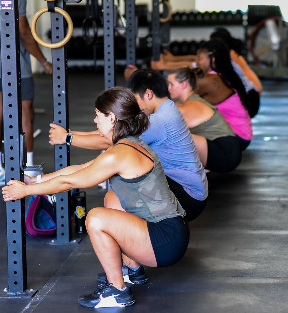 Athletes performing synchronized squats at a rack during group training session.