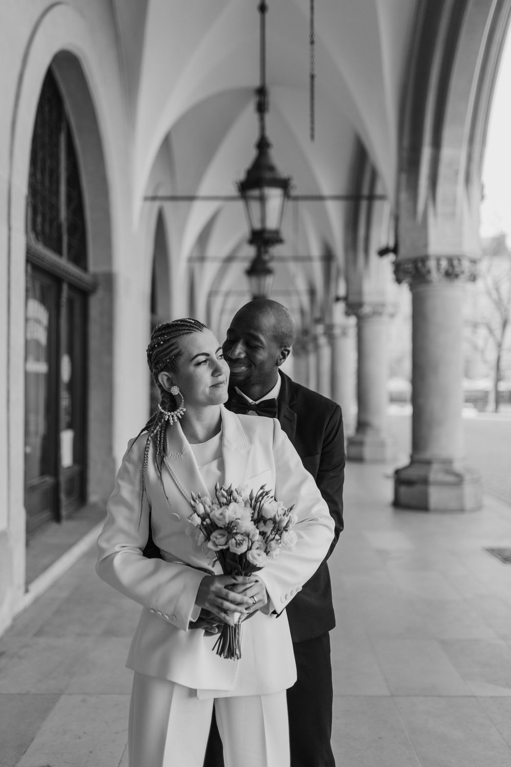 Black and white portrait of couple with bouquet under historic colonnade.