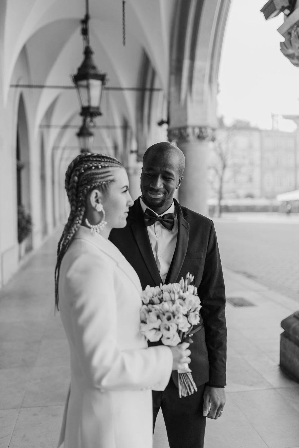 Black and white portrait of couple sharing intimate moment in historic arcade.