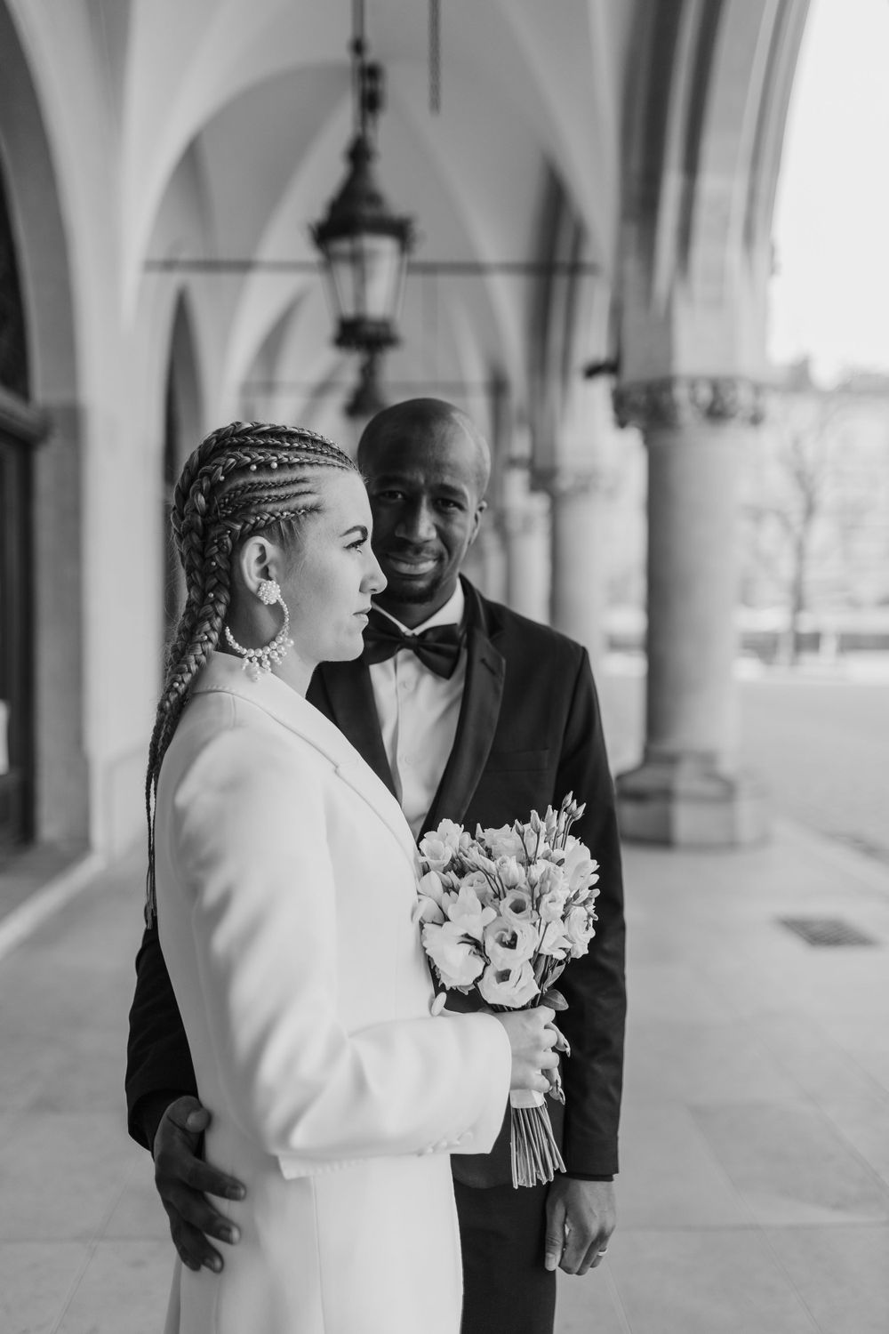 Black and white wedding photo in architectural colonnade with white bouquet.