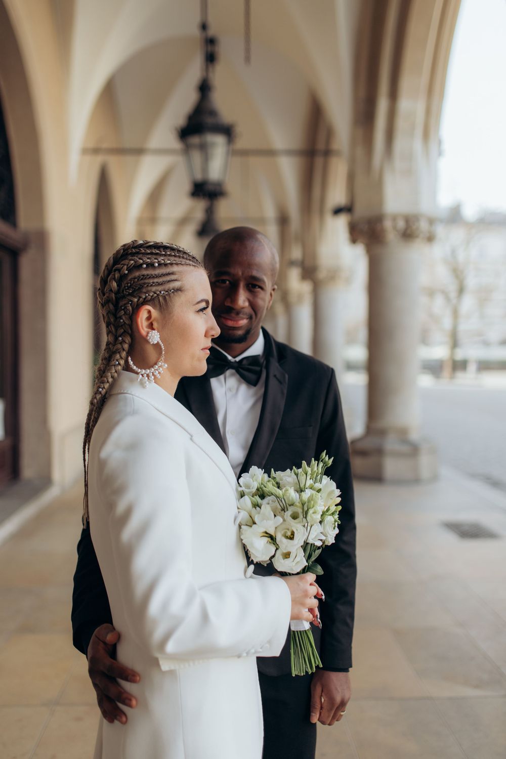 Wedding portrait under arched colonnade with white floral bouquet.