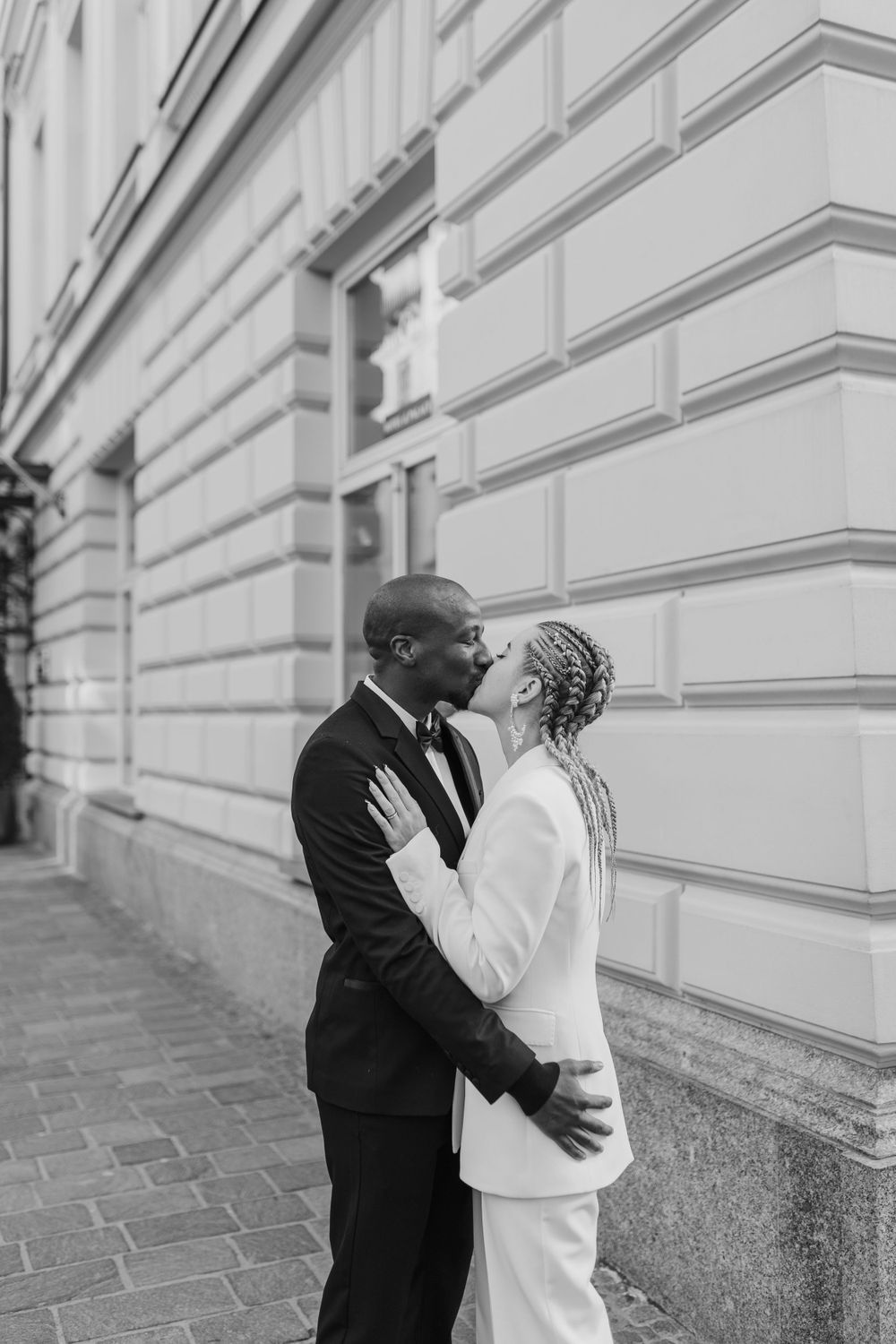 Black and white portrait of couple sharing romantic moment against classic building facade.