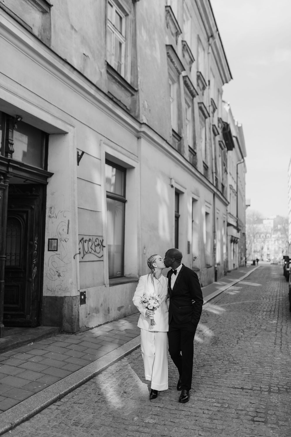 Black and white photo of couple walking along historic cobblestone street.