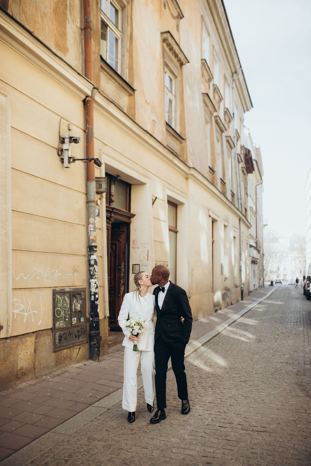 Couple standing together on cobblestone street beside historic building facade.