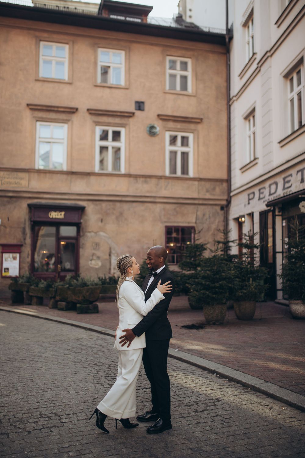 Couple embracing on cobblestone street surrounded by classic European architecture.