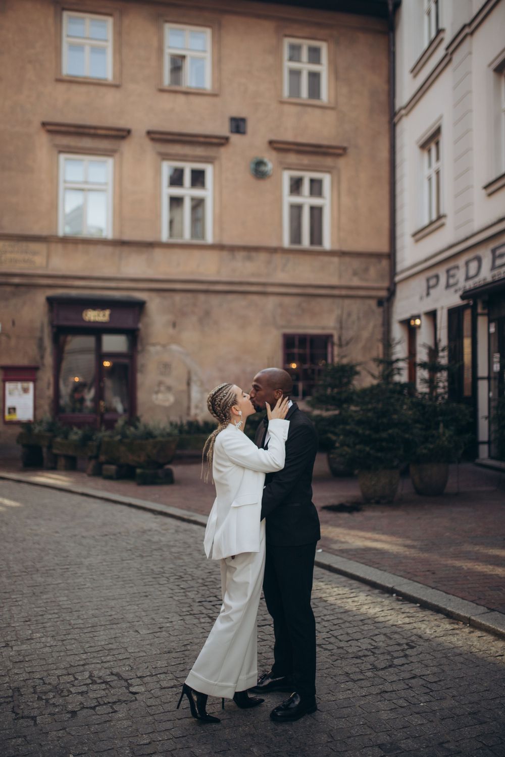 A couple in formal wear dances on cobblestone streets outside historic buildings.