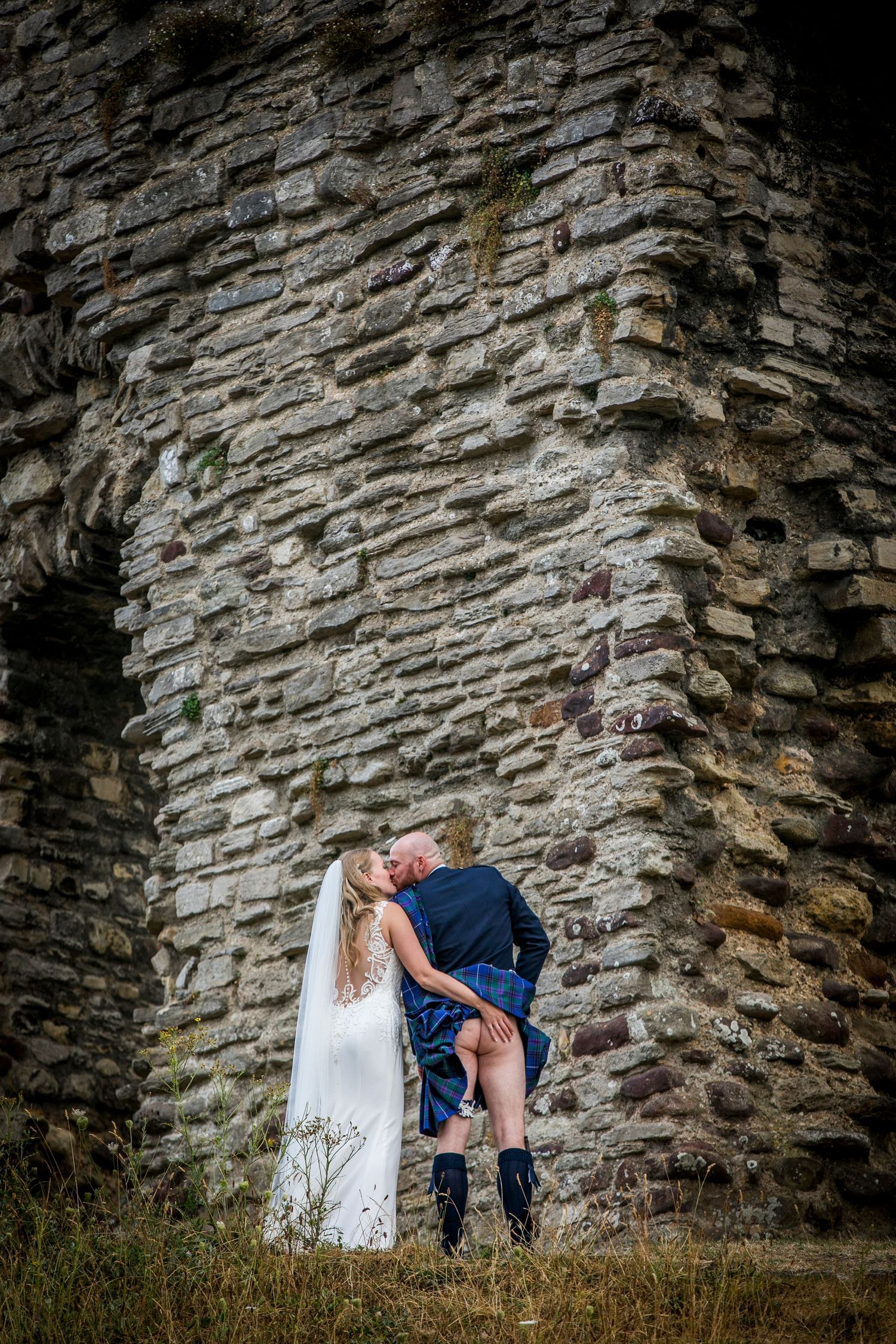 A romantic moment captured against a textured stone wall in a dramatic outdoor setting.