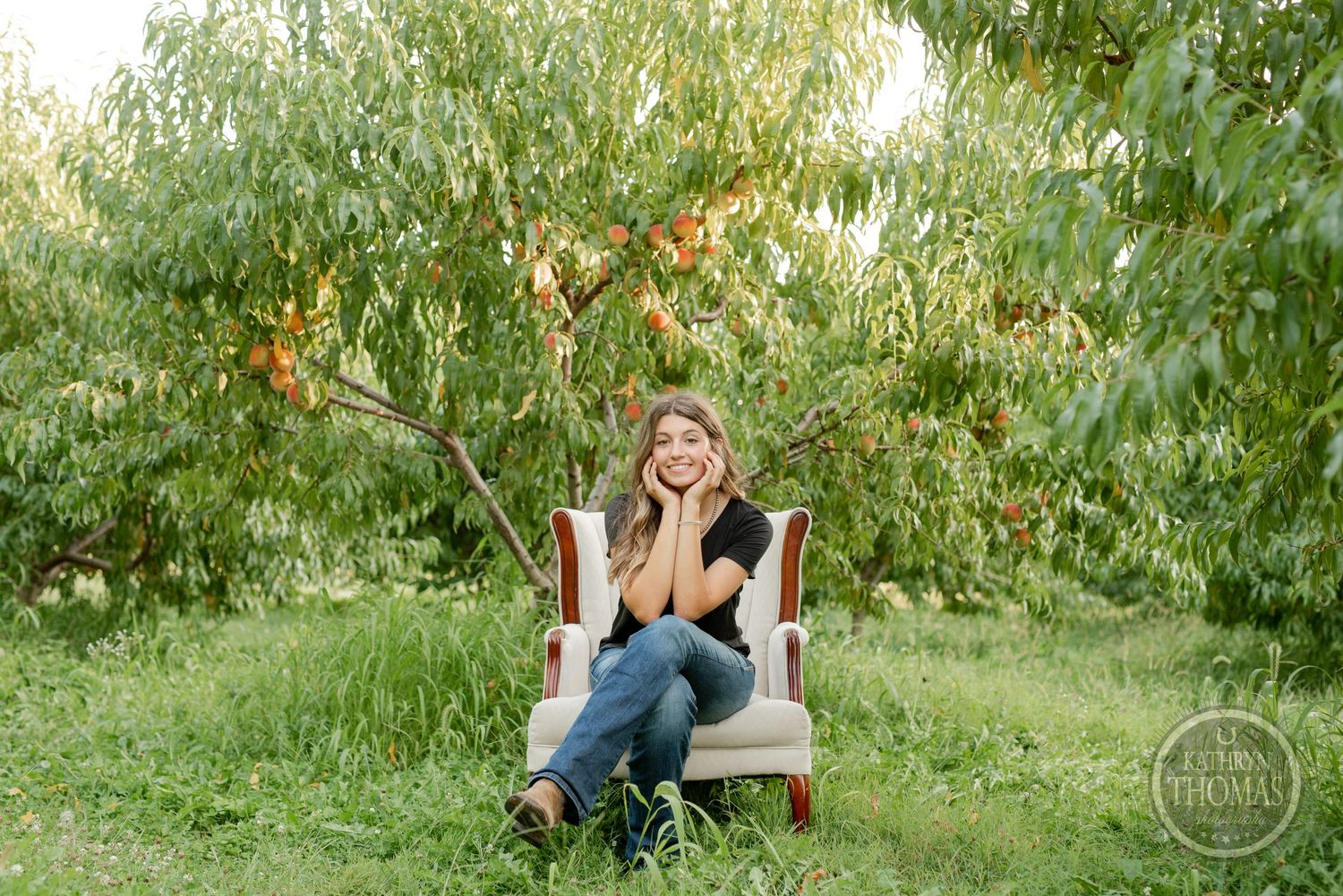 Candid portrait in a white chair surrounded by peach trees in a garden setting.
