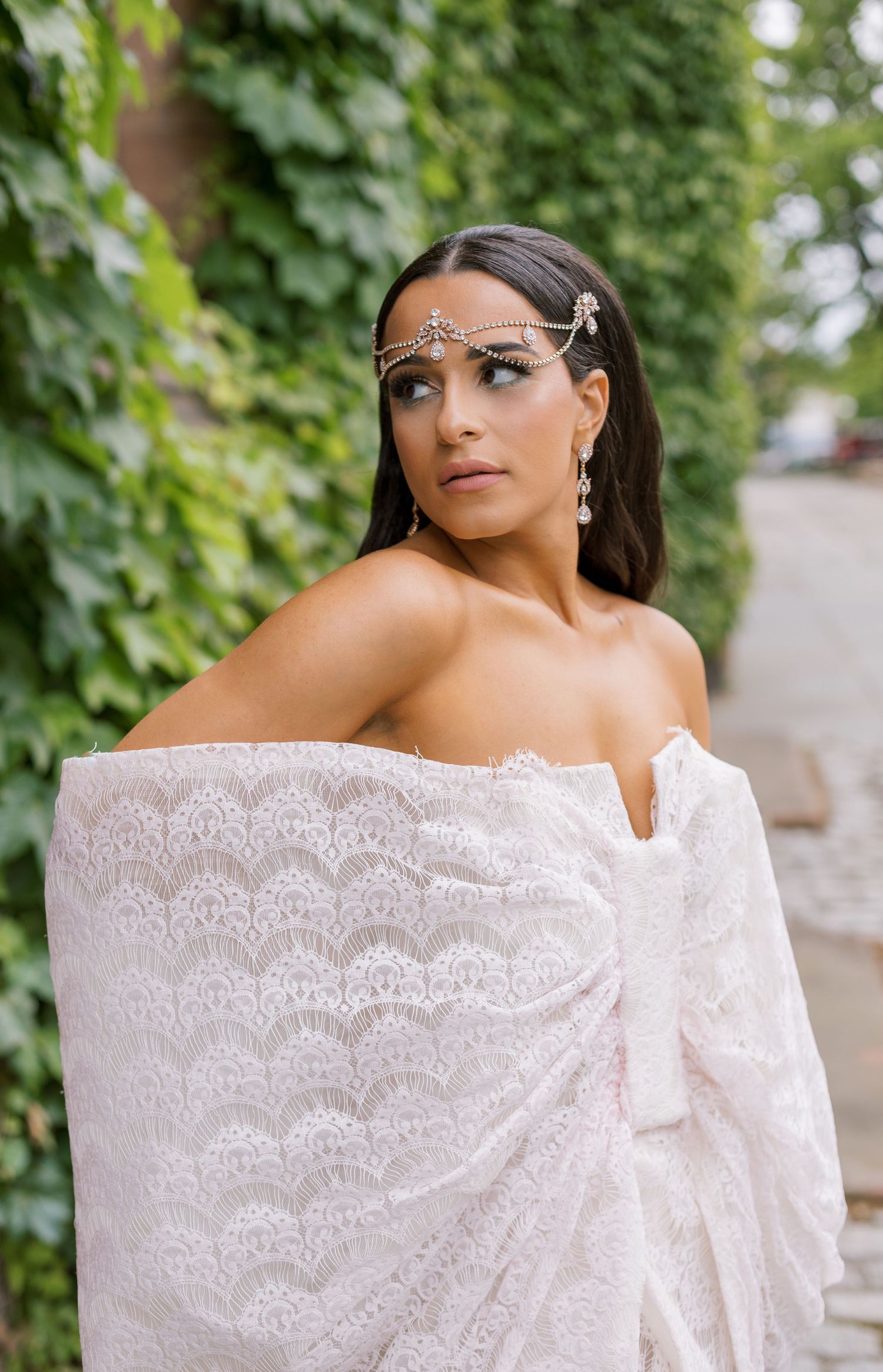 Fashion portrait featuring delicate face jewelry and off-shoulder white lace dress.