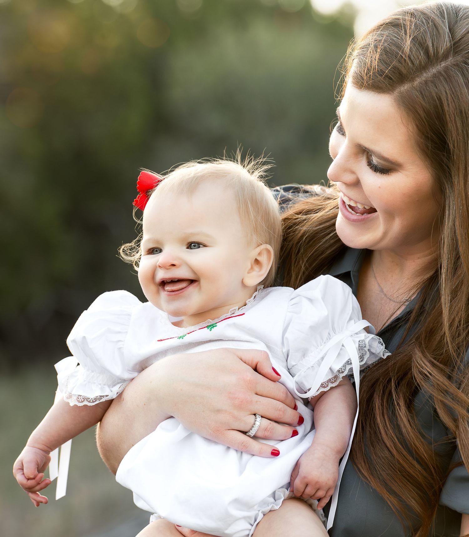 a mother holds her infant daughter close and looks at her with a big smile as the infant sticks out her tongue and smile
