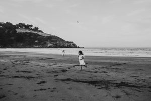 A solitary figure in white walks along a misty beach with cliffs in the background.