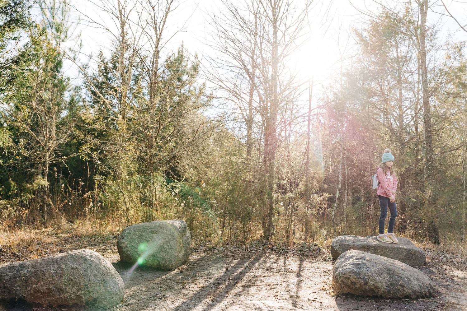 young girl stands on large rock with blue winter hat in Charlotte NC nature preserve