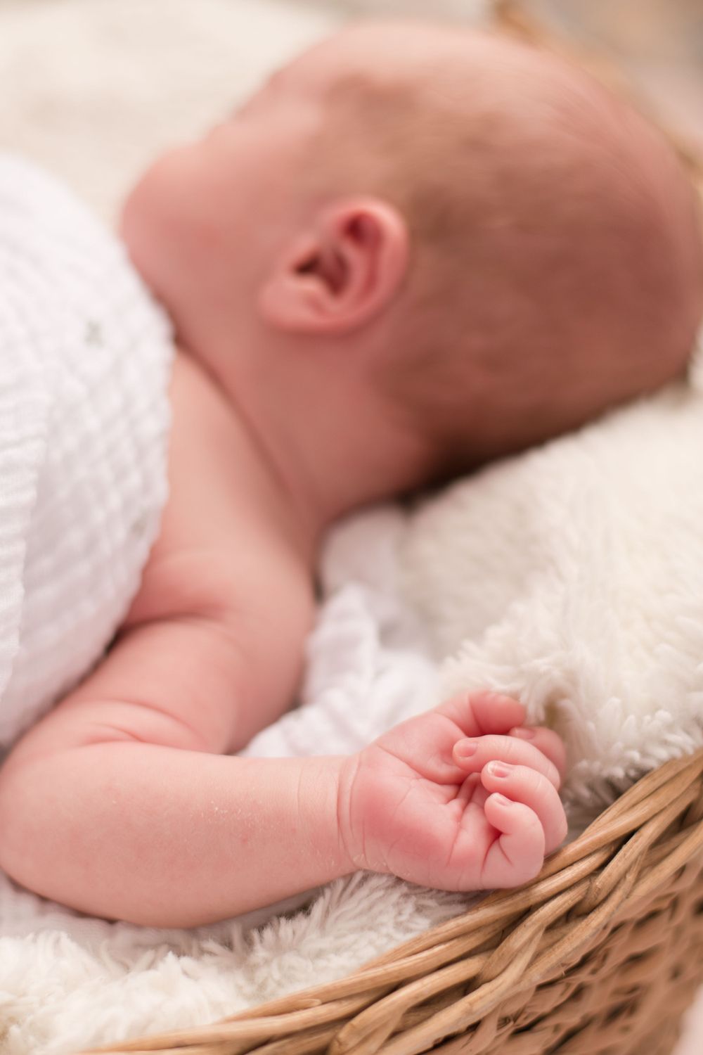 little one wrapped in blanket and looking away. His hand is the focus and laying near the edge of his basket.