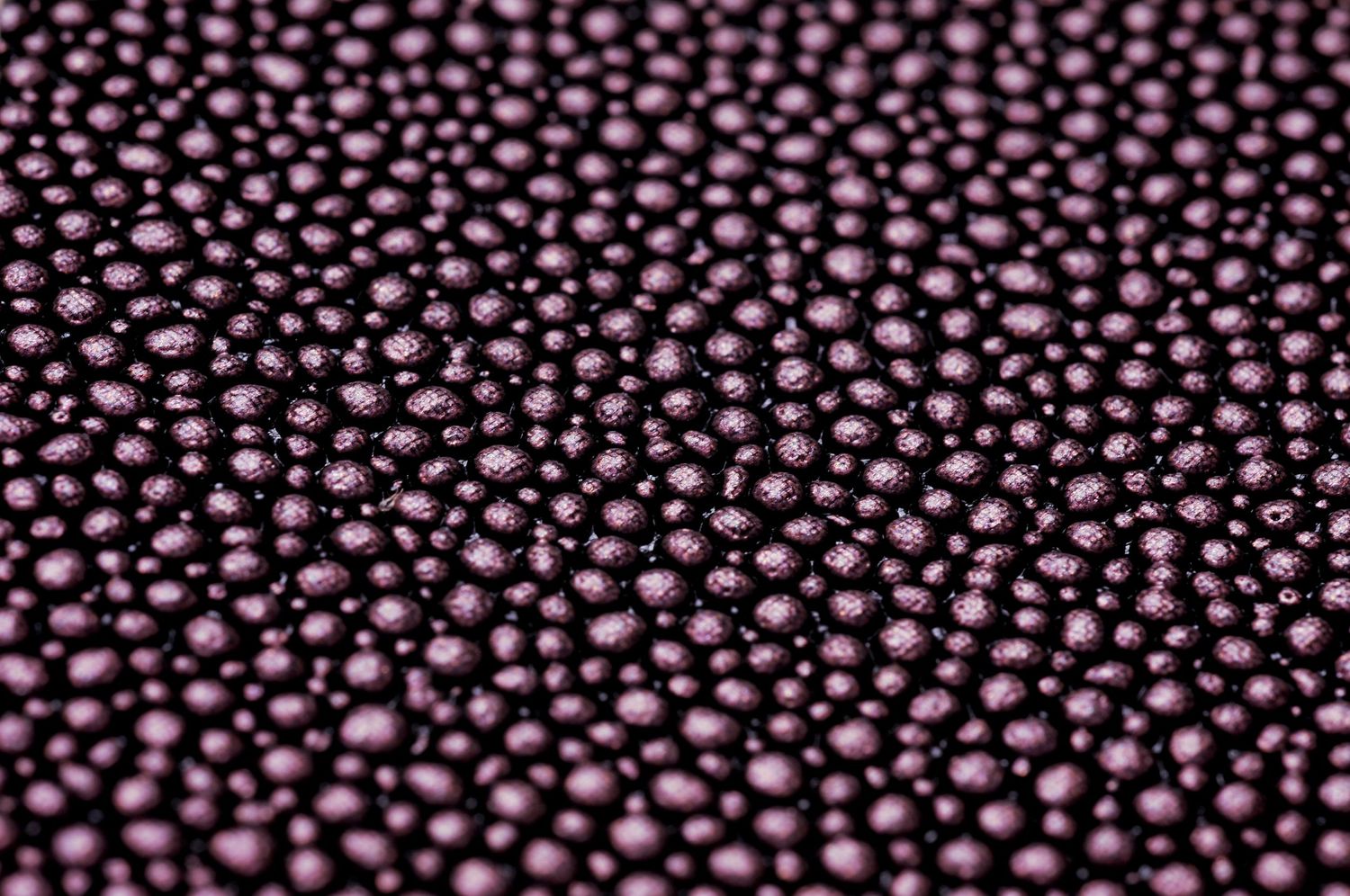 Close-up macro shot of metallic purple beads or ball bearings creating a repeating pattern texture.