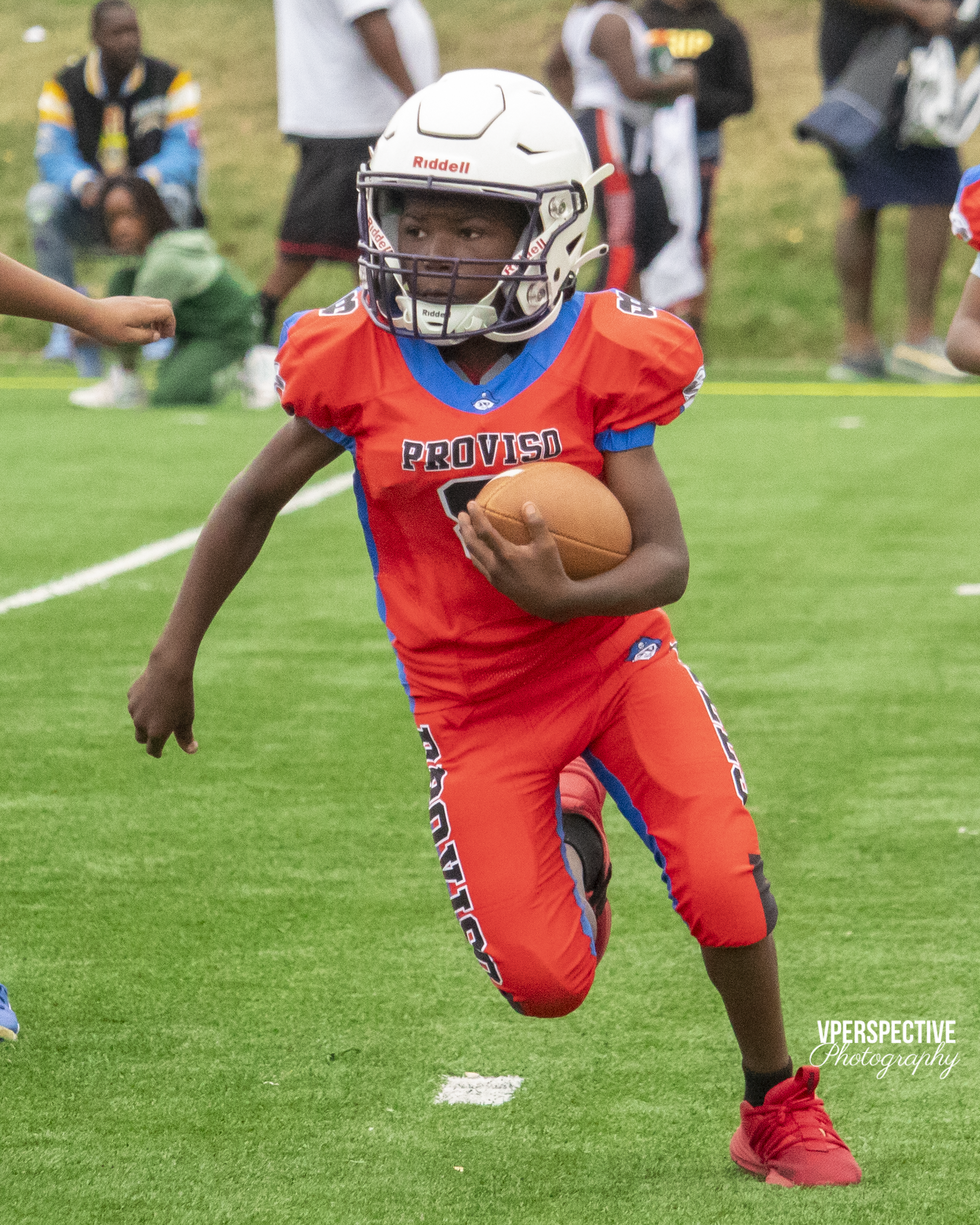 Youth football player in red uniform carries ball during game.