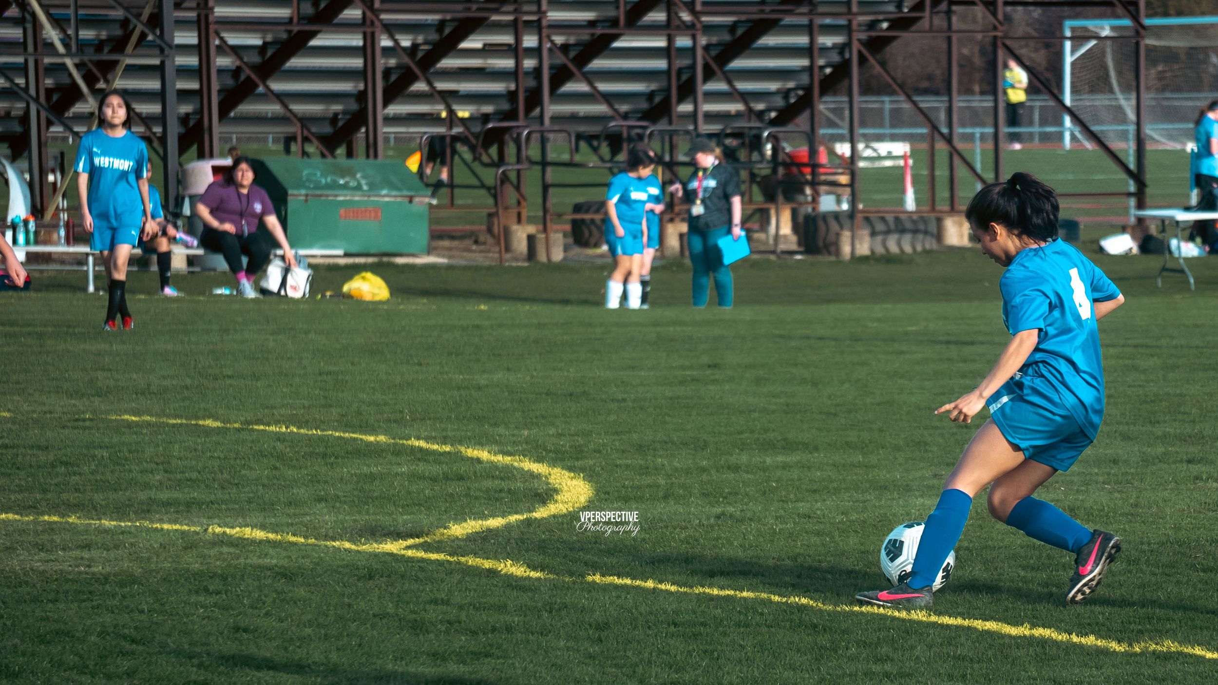 Soccer players in bright blue uniforms practice on a field with yellow markings.