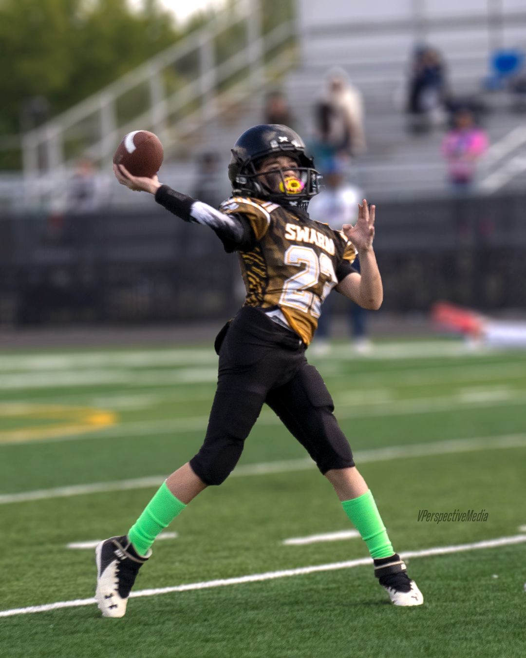 Youth football player in black and gold uniform throws a pass on the field.