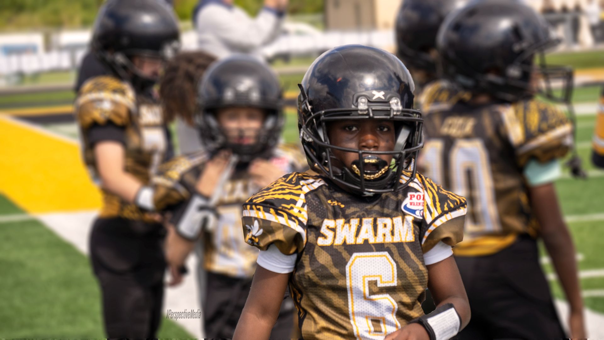 Youth football players in black and gold uniforms with SWARM text on field.