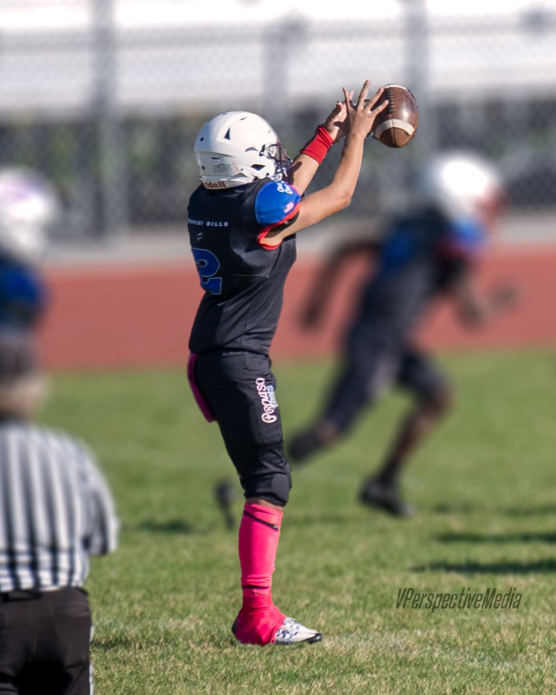 Football player in black jersey and pink socks catches the ball during practice.
