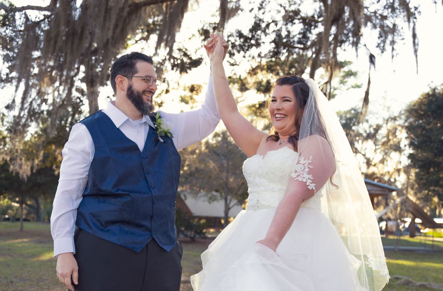 Wedding couple poses amid moss-draped trees at sunset during outdoor ceremony.