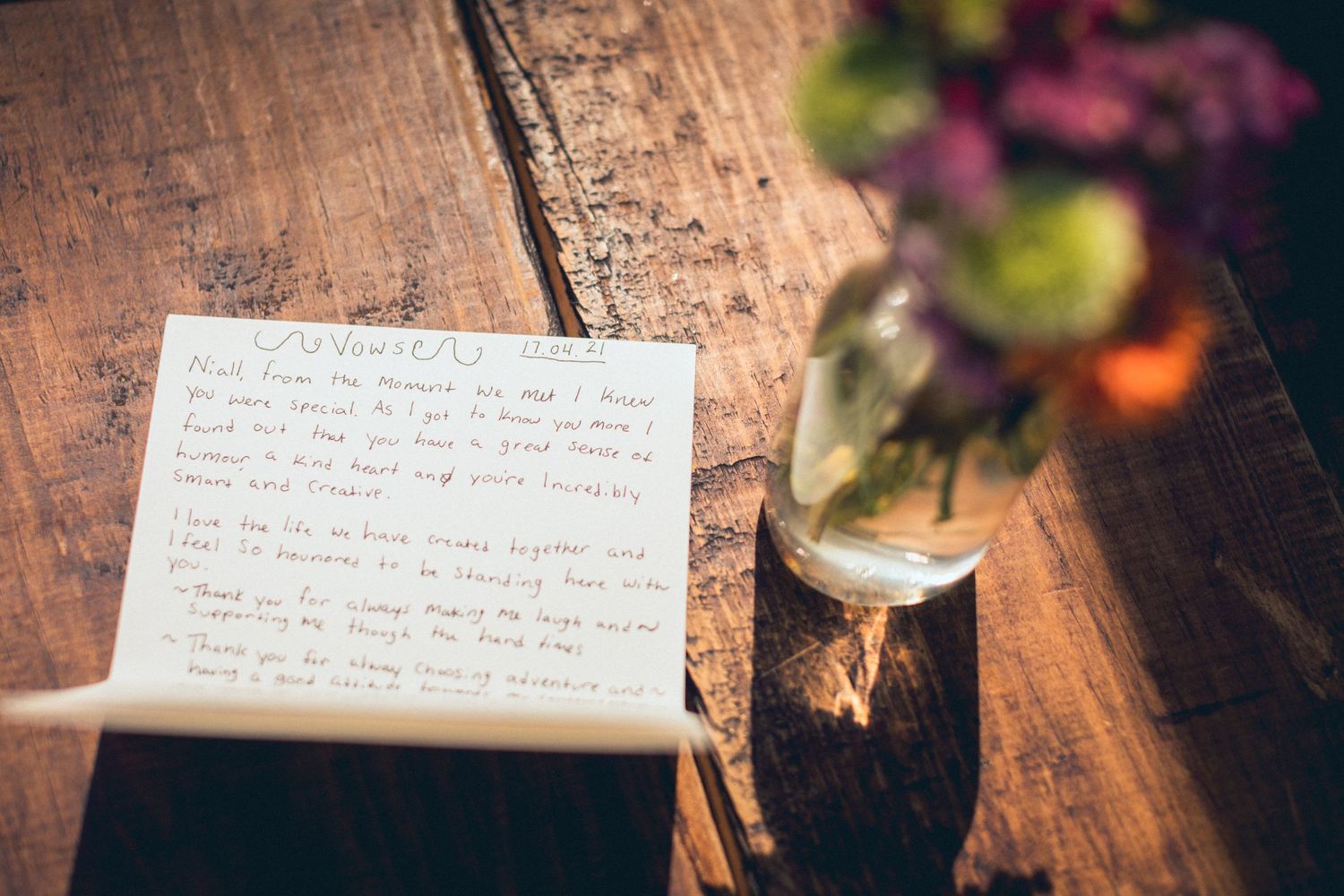 Handwritten notes on rustic wooden table with flowers in background.