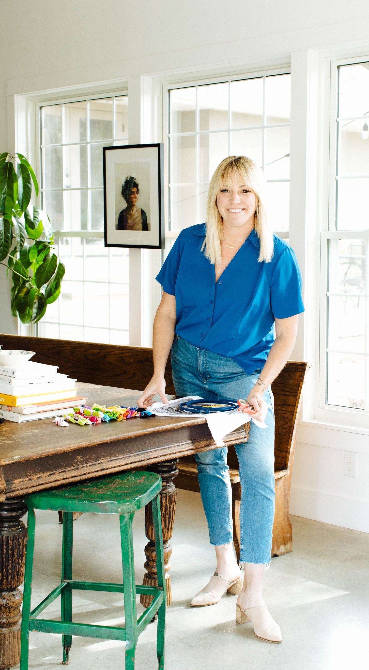 Woman in blue shirt sitting on rustic green bench in bright white room with windows.