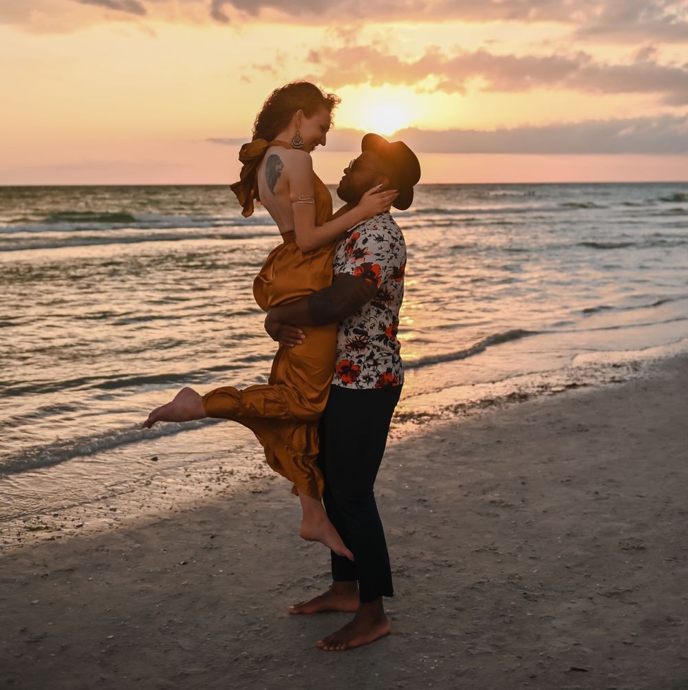 Romantic couple embraces on beach at sunset with ocean waves in background.