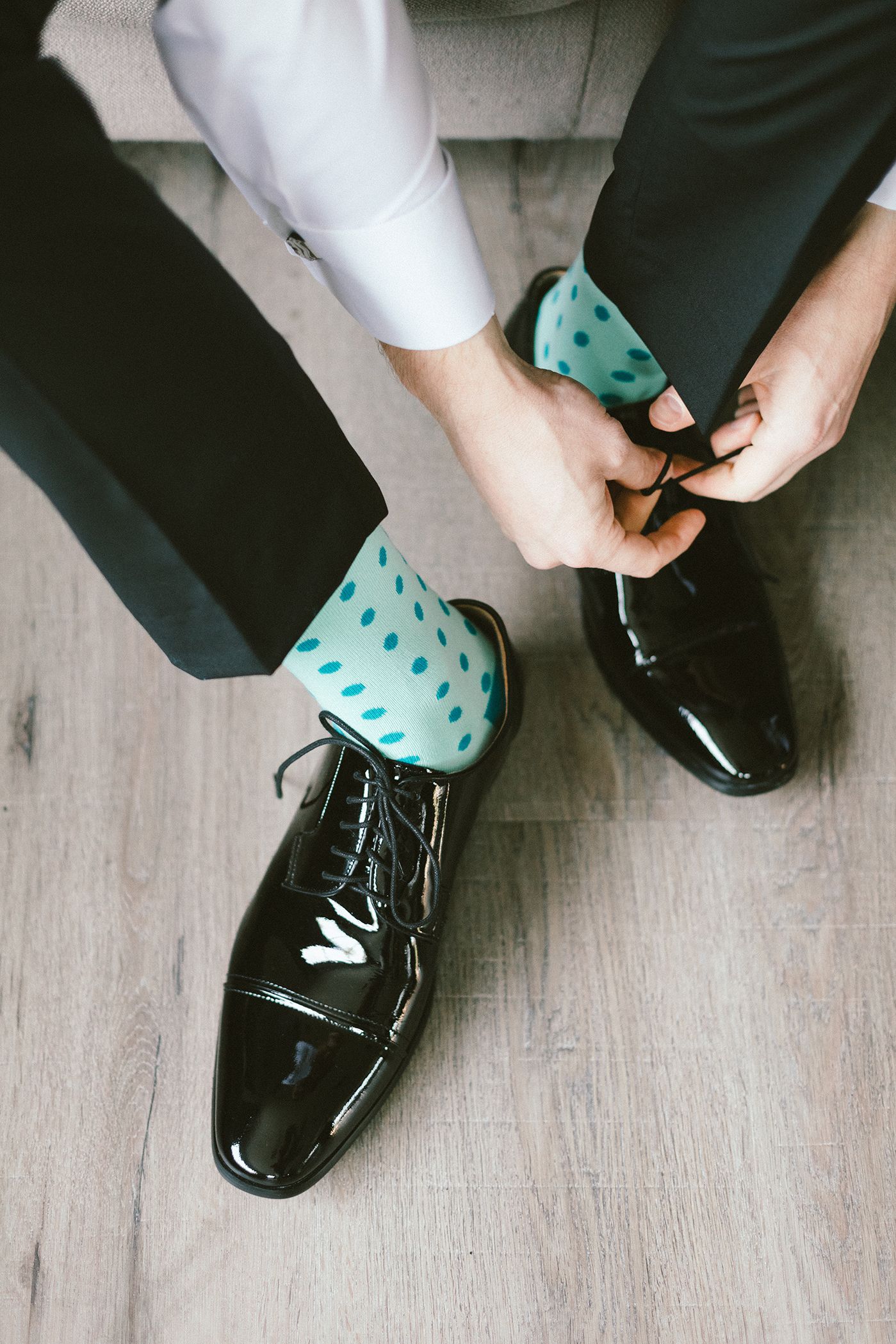 Close-up of polished black dress shoes with teal polka dot socks being tied.