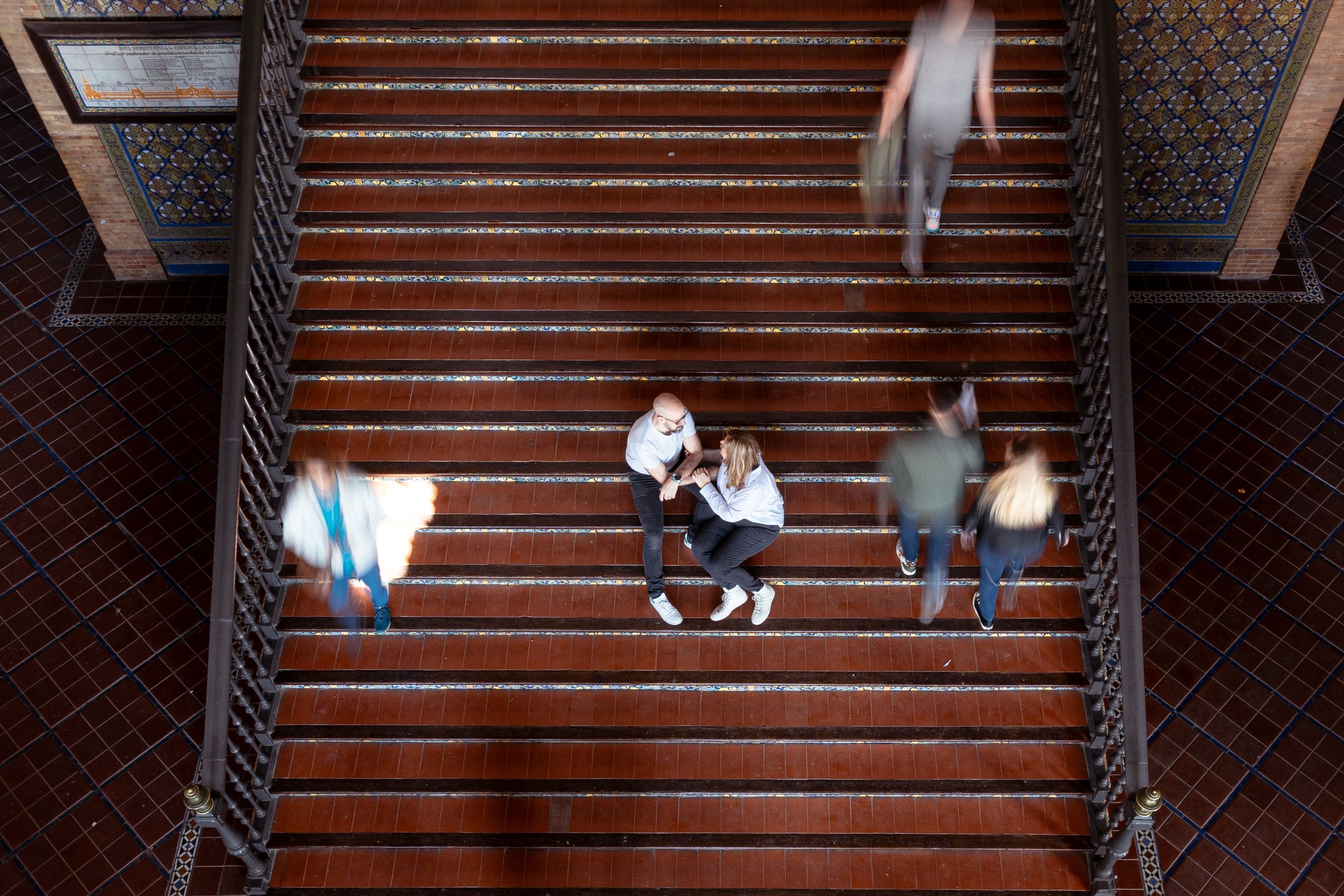 Birds-eye view of people walking on wooden stairs with decorative railings.