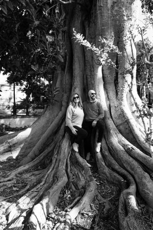 Black and white photo of couple sitting on massive tree roots in a park setting.