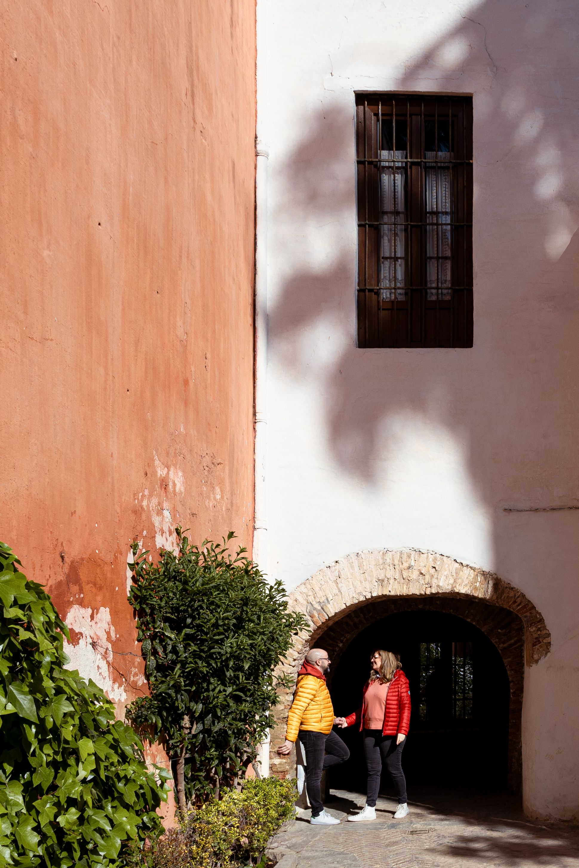 Architectural detail of a Spanish courtyard with pink walls, shadows, and a traditional window.