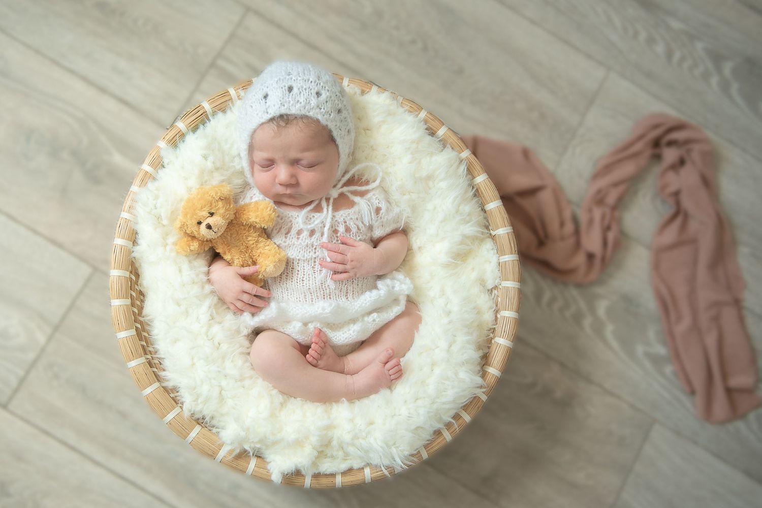 Newborn baby girl in knitted white frilly dress romper in basked with teddy, newborn photographer Ashford, Kent. Studio