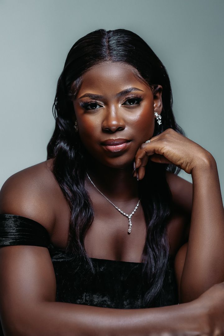 Glamorous portrait in black off-shoulder dress with diamond necklace against gray background.