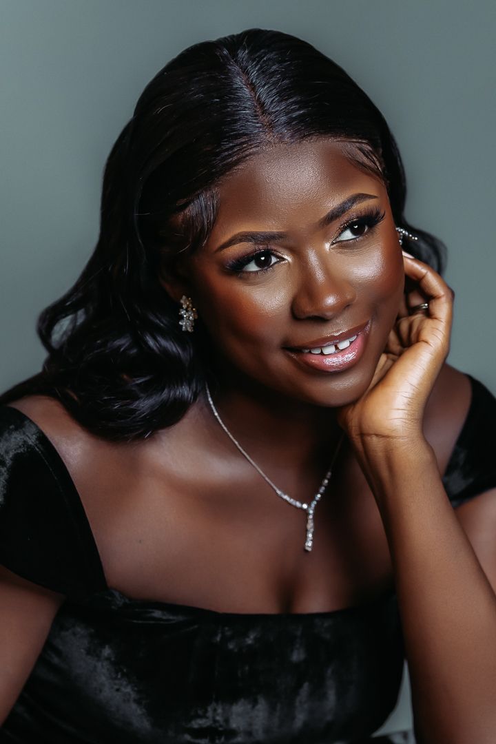 Elegant portrait featuring black velvet dress and delicate jewelry against gray backdrop.