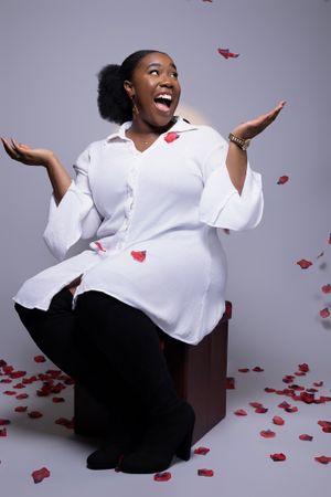Joyful studio portrait with white shirt and falling red rose petals against gray background.
