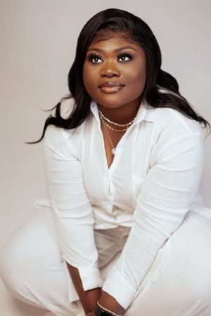 Elegant portrait with white button-down shirt and layered necklaces against light background.