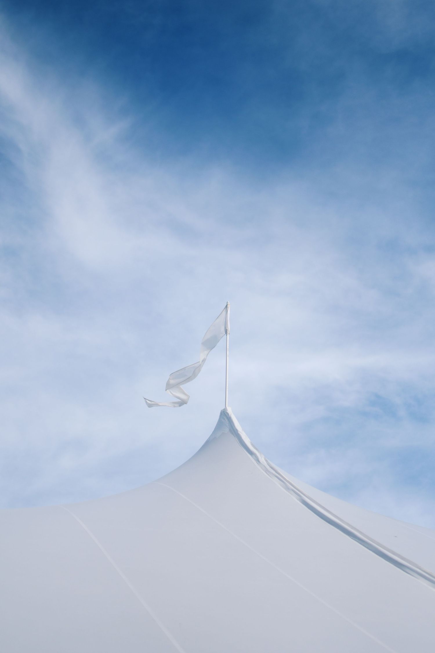 White event tent peak against blue sky with flag waving in the breeze.