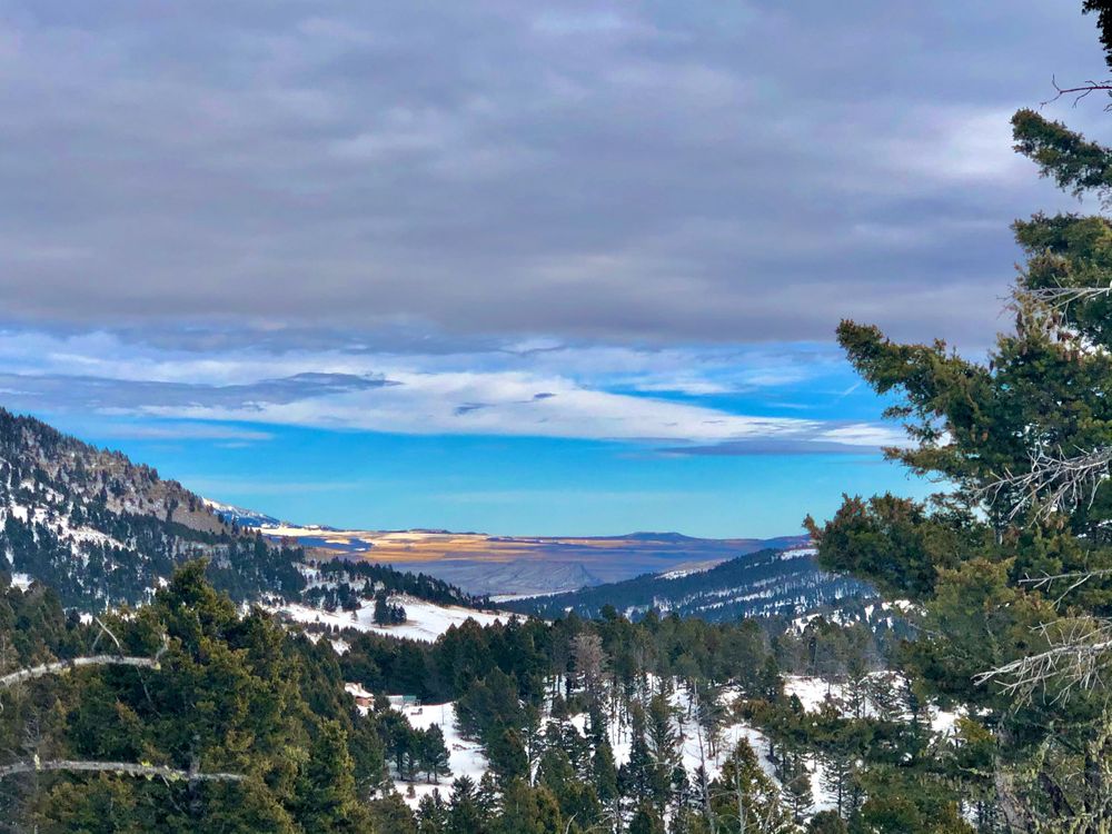 Snow-covered mountain vista with bright blue sky peeking through dramatic clouds.