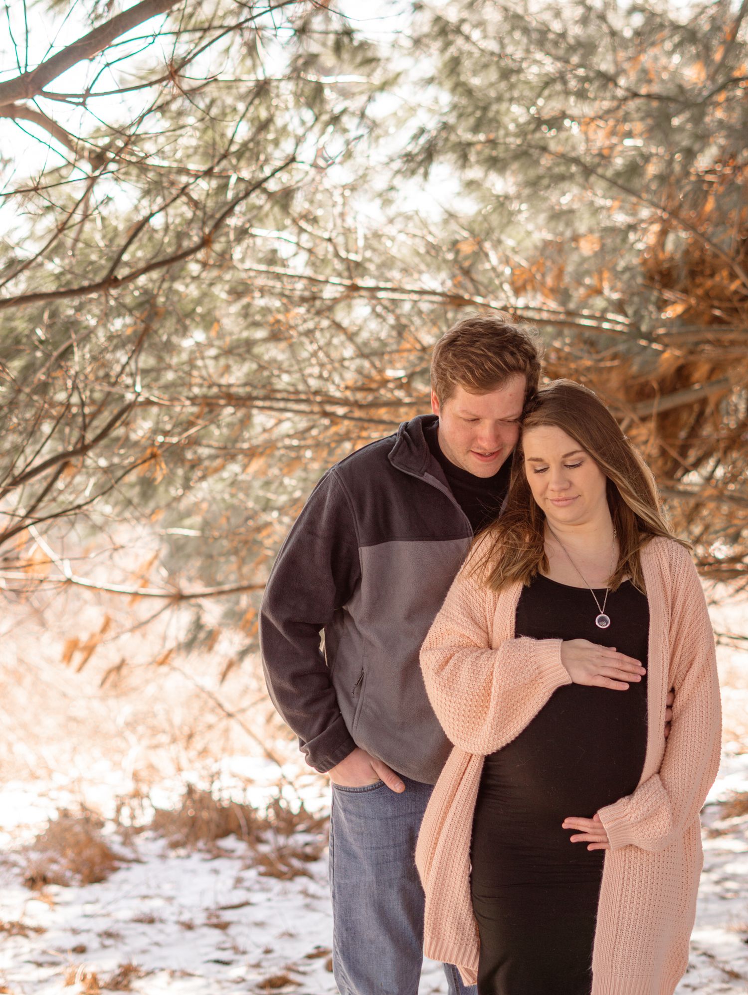 Expectant couple in winter scene with snow and trees.