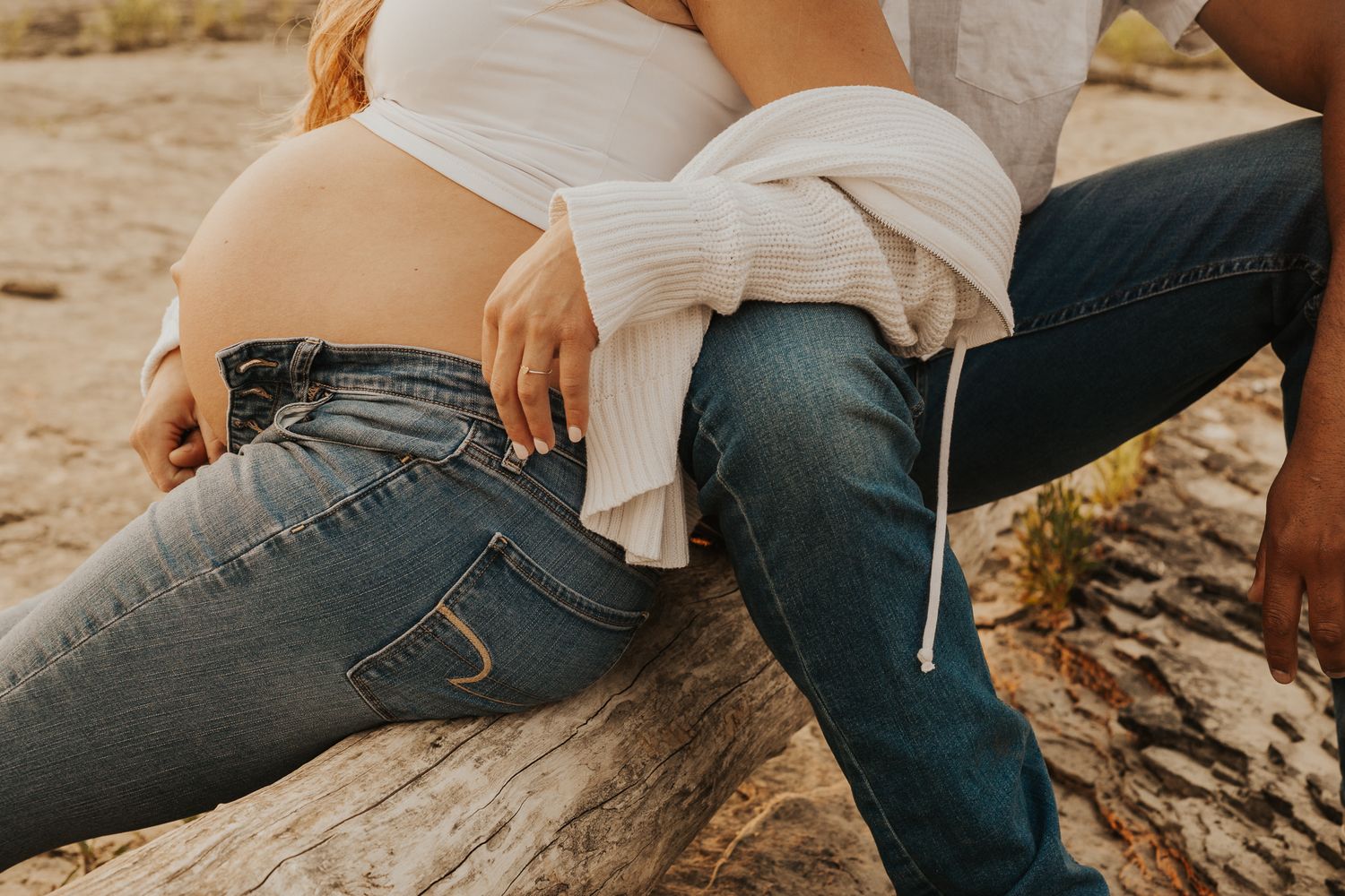 Close-up shots of couple sitting on rocky ground in casual denim and white attire.