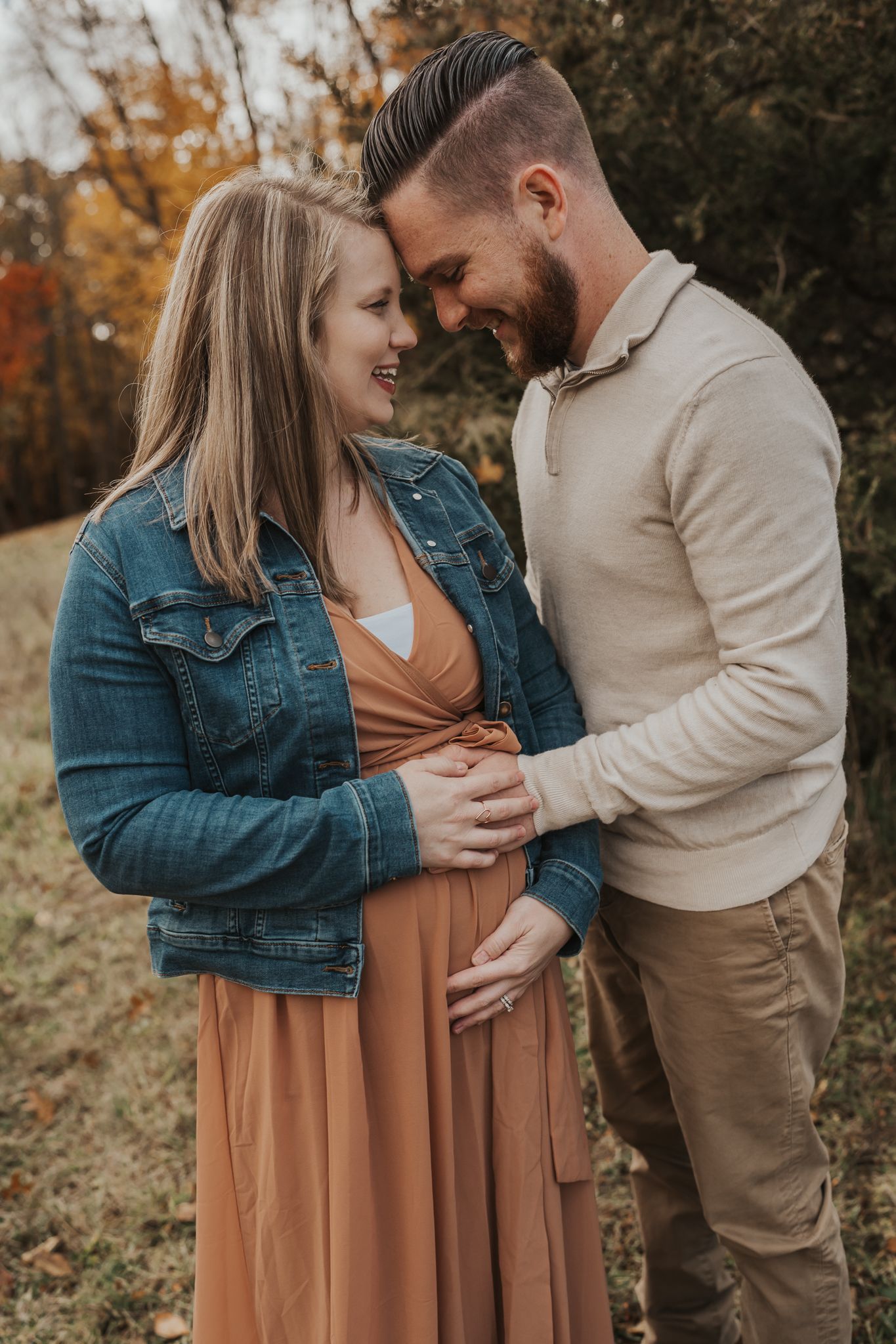 Couple sharing intimate moment during fall maternity photoshoot in nature setting.