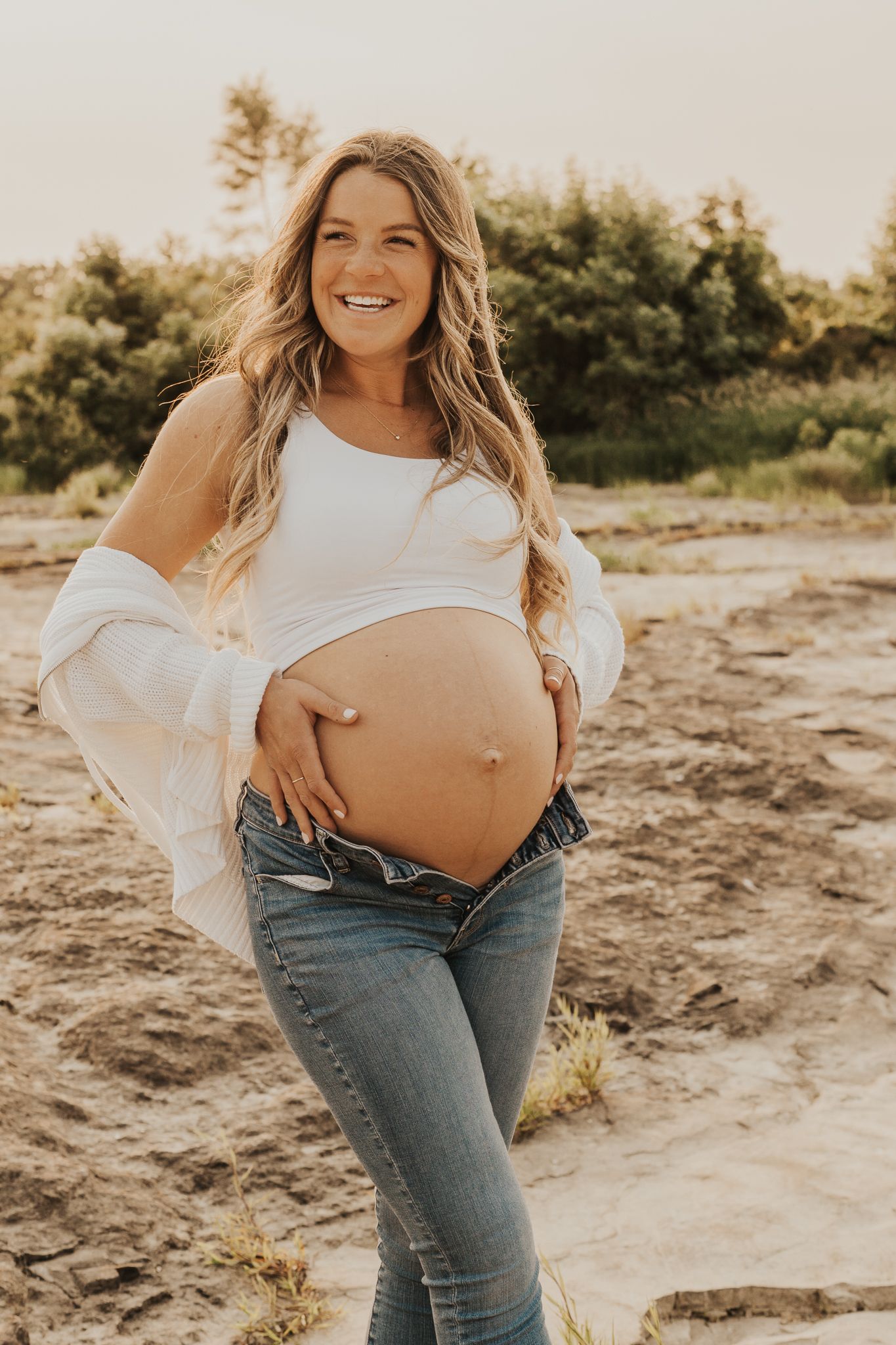 Maternity photo of expectant mother in casual attire on sandy beach in Michigan.